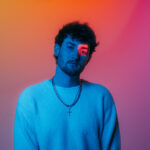 Austin Snell in a promotional portrait lit with blue, pink, and orange light.