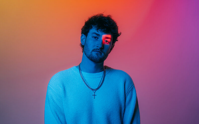 Austin Snell in a promotional portrait lit with blue, pink, and orange light.