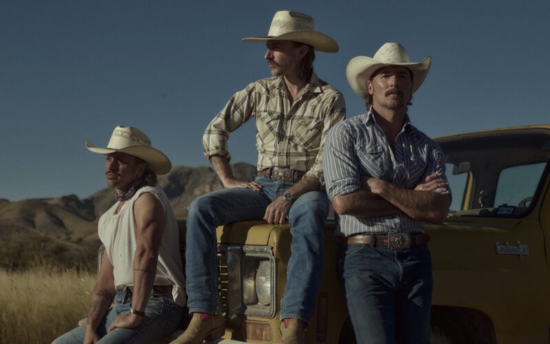 Midland band members in cowboy hats standing beside a yellow vehicle in the desert.